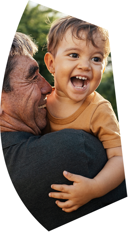 An older man smiling and holding a toddler who is looking toward the camera and smiling with his mouth open